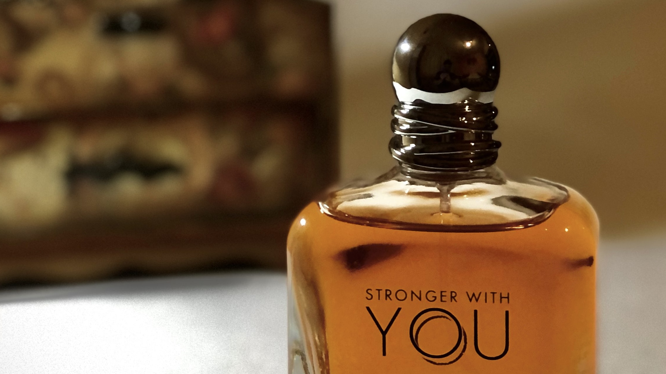 Armani Stronger With You Intensely: orangefarbener Flakon mit Schriftzug vor unscharfem Hintergrund