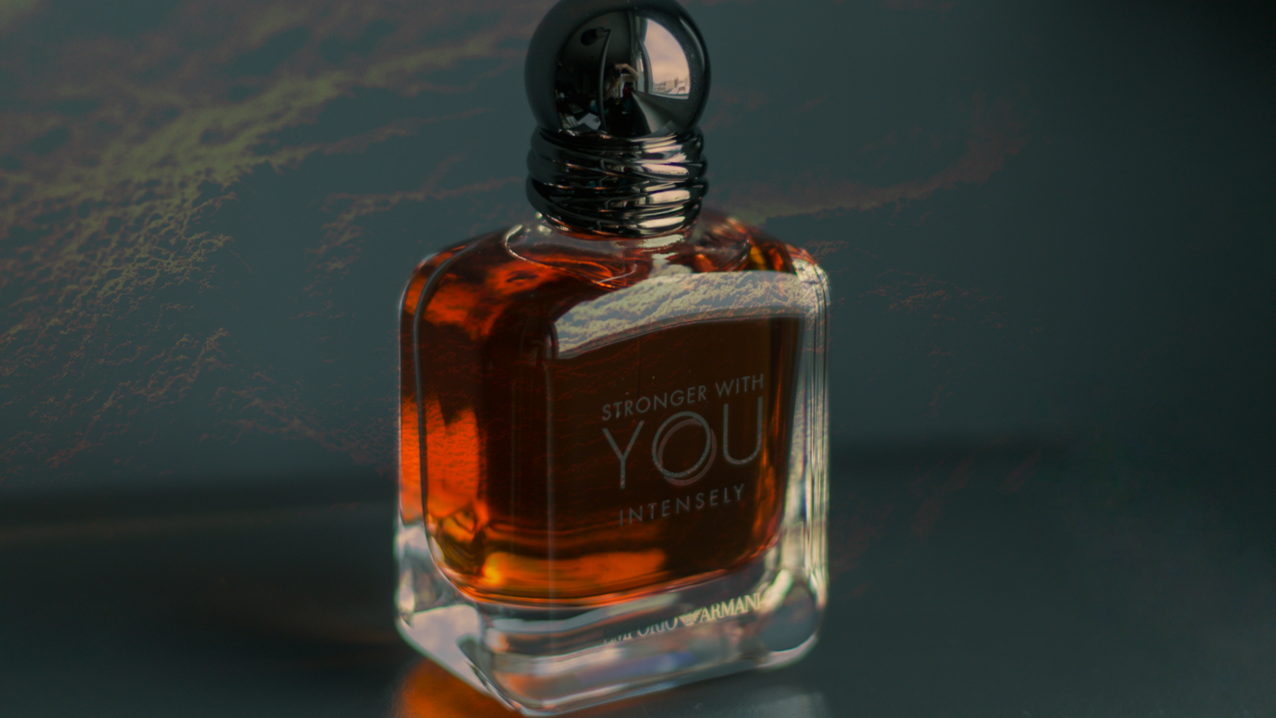 Armani Stronger With You Intensely vs Azzaro The Most Wanted: Flakon von Stronger With You Intensely vor dunkelgrünem Hintergrund