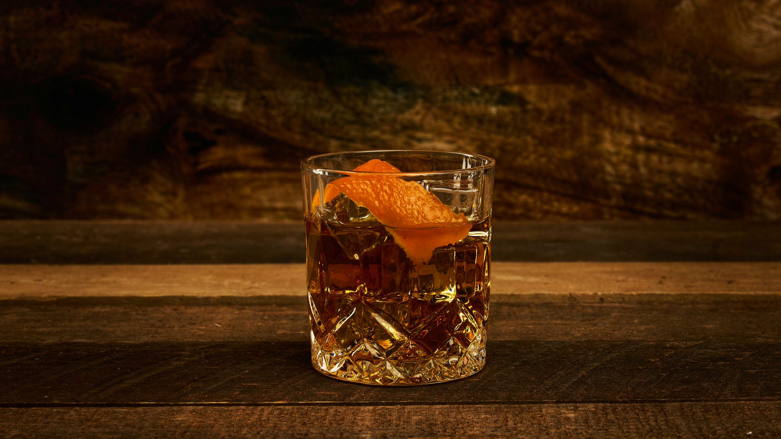 DICK JOHNSON Serpent: Tumbler mit bernsteinfarbenem Drink und Orangenzeste auf dunklem Holz