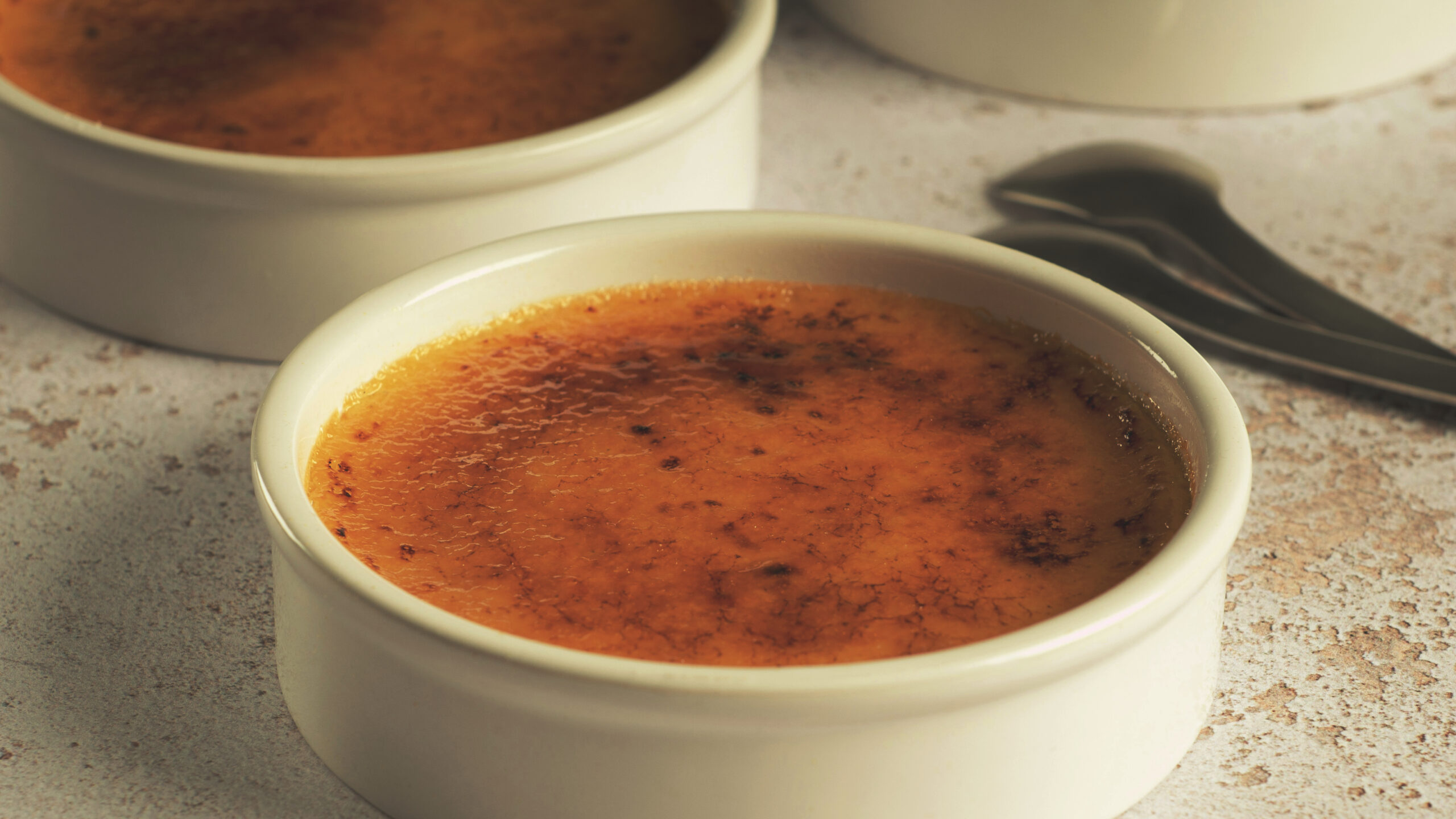 Lattafa Honor und Glory: Crème brûlée mit karamellisierter Kruste in weißen Förmchen auf Stein