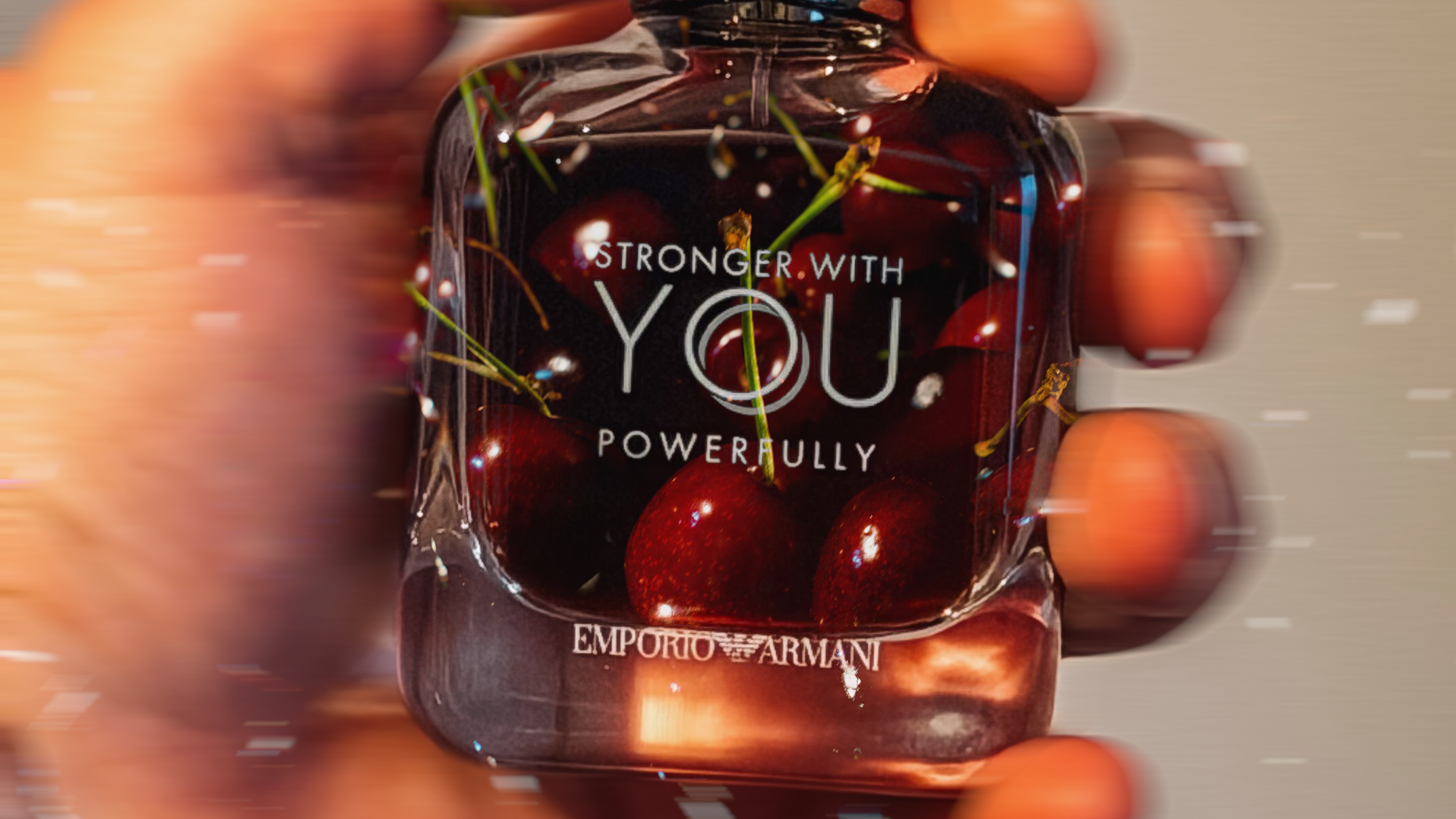 Armani Stronger With You Powerfully: Flakon in einer Hand, darin dunkelrote Kirschen, mit Bewegungsunschärfe