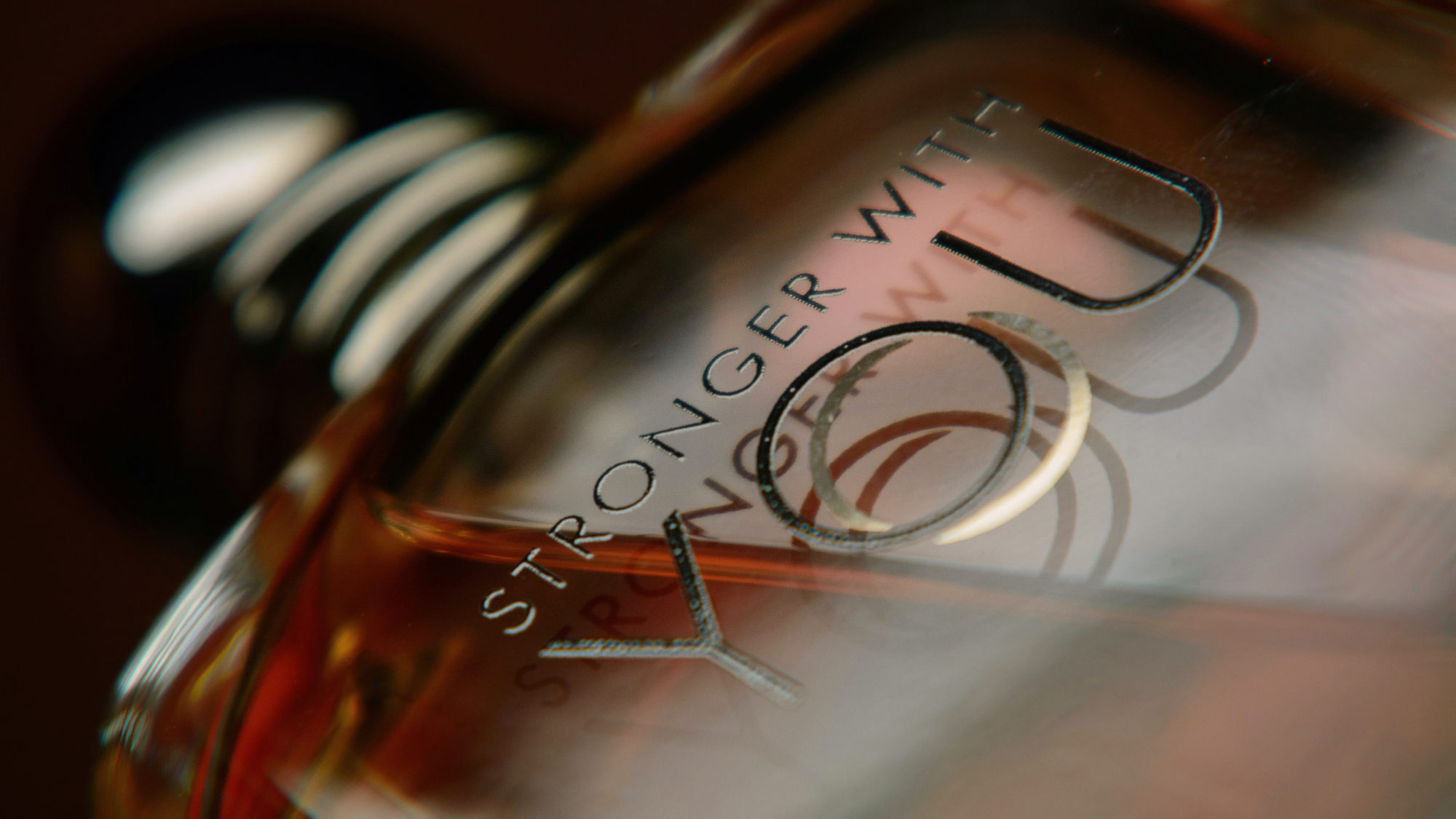 Armani Stronger With You Absolutely: Nahaufnahme des Flakons mit eingravierter Schrift in warmem Bernsteinlicht